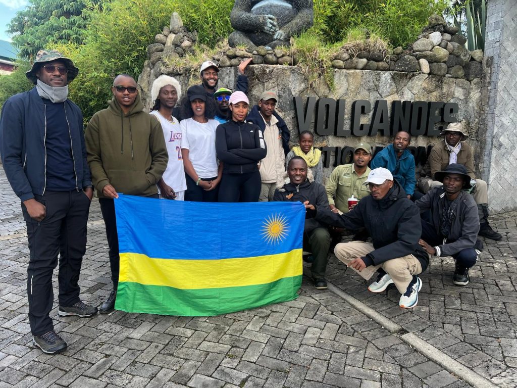 Group of Explore More Tours clients posing at the Visit Rwanda and Volcanoes National Park sign