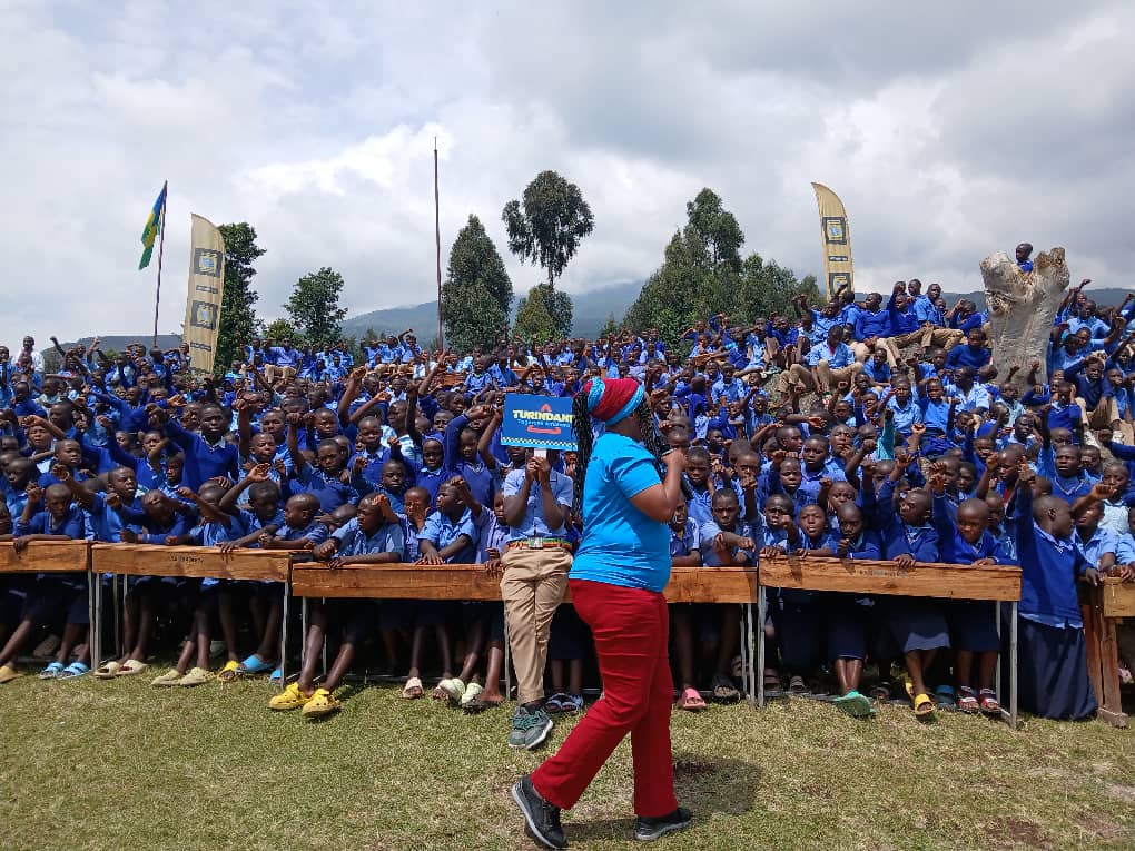 The Fight Against Drug Abuse: A woman named Marie Claire Uwineza, also known as MUTIMAWURUGO Claire, stands in front of many young people in Rwanda. She holds a microphone and speaks passionately during a campaign to fight drug abuse. The crowd listens attentively. The scene shows youth engagement, community awareness, and the fight against drug abuse in Rwanda.